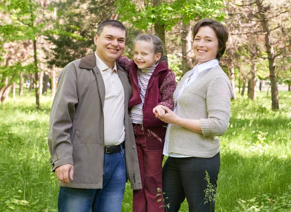Família feliz com criança no parque de verão, luz solar, grama verde e árvores — Fotografia de Stock