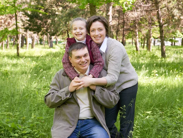 Família feliz com criança no parque de verão, luz solar, grama verde e árvores — Fotografia de Stock