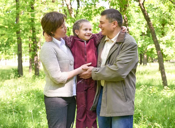 Šťastná rodina s dítětem v létě park, sluneční světlo, zelené trávy a stromy — Stock fotografie
