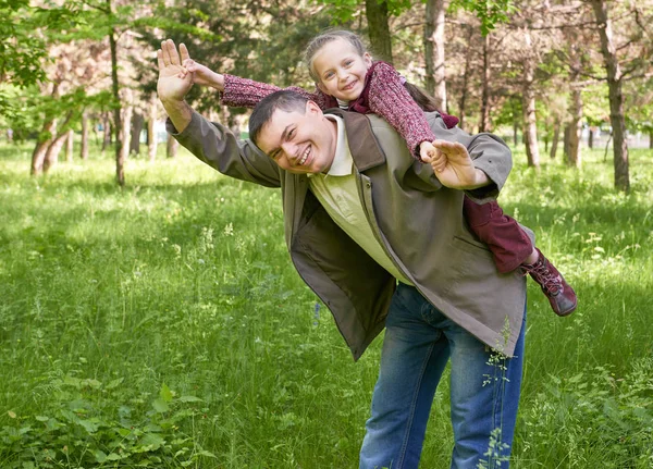 Father playing with child girl in summer park, sunlight, green grass and trees — Stock Photo, Image