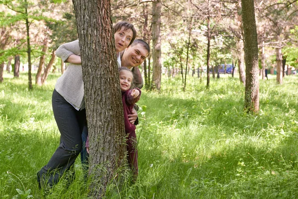 Gelukkige familie en kind in de zomer park. Mensen verbergen en speelt achter een boom. Mooi landschap met bomen en groen gras — Stockfoto
