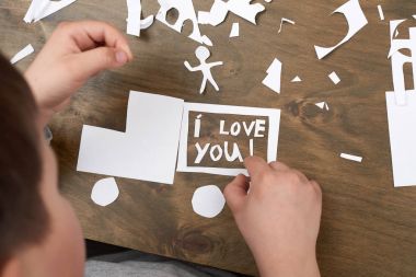 boy makes origami - car and family, children, parent, I love you text, top view on wood background clipart