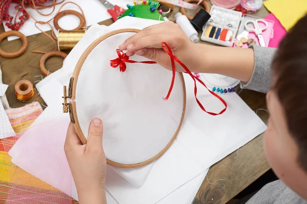 Boy embroidered on the hoop, hand closeup and red ribbon on white textile, learns to sew, job training, handmade and handicraft concept — Stock Photo, Image