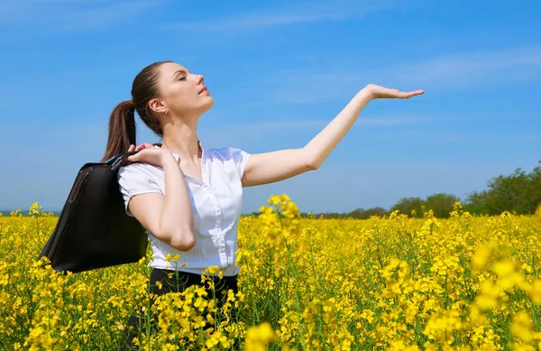 Geschäftsfrau mit Aktentasche zeigt Handfläche zur Sonne. junges Mädchen im gelben Blumenfeld. schöne Frühlingslandschaft, strahlend sonniger Tag, Raps — Stockfoto