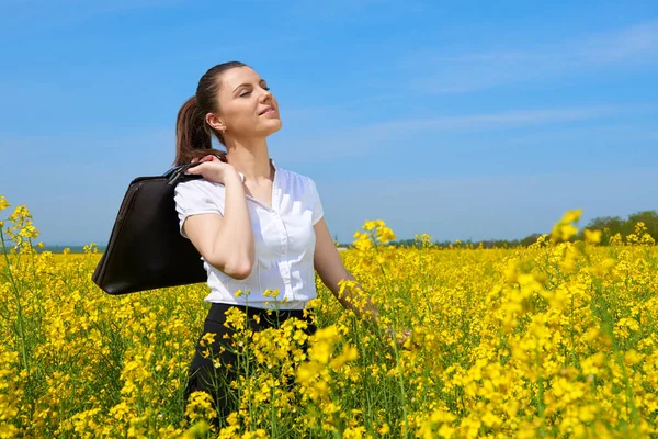 Geschäftsfrau mit Aktentasche entspannt sich im Blumenfeld unter der Sonne. junges Mädchen im gelben Rapsfeld. schöne Frühlingslandschaft, strahlend sonniger Tag — Stockfoto