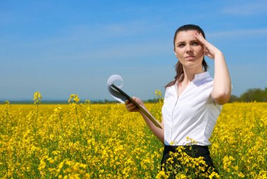 Business woman in flower field outdoor with clipboard look into the distance. Young girl in yellow rapeseed field. Beautiful spring landscape, bright sunny day clipart