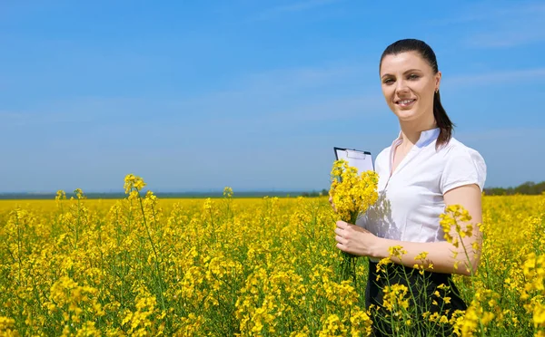 Obchodní žena s kyticí a schránky, které jsou v květu pole venkovní relaxační. Mladá dívka v žlutou řepkové pole. Krásný Jarní krajina, jasný slunečný den — Stock fotografie