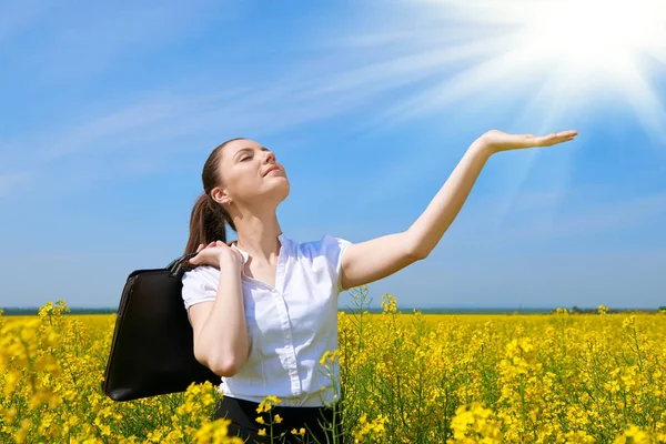 Zakenvrouw met werkmap ontspannen in bloem veld buiten onder de zon. Jong meisje in het geel koolzaad veld. Prachtige lente landschap, zonnige dag — Stockfoto