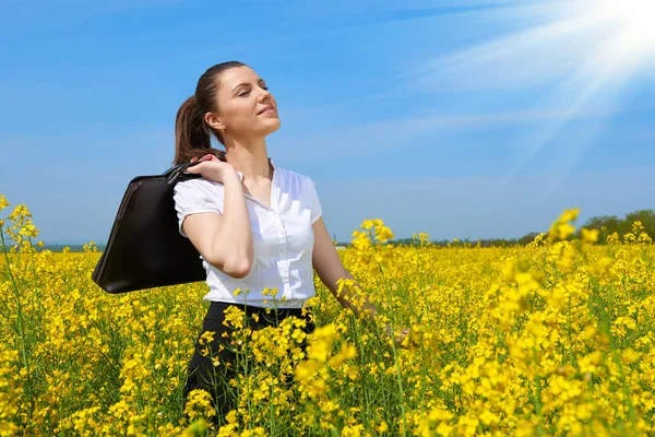 Zakenvrouw met werkmap ontspannen in bloem veld buiten onder de zon. Jong meisje in het geel koolzaad veld. Prachtige lente landschap, zonnige dag — Stockfoto