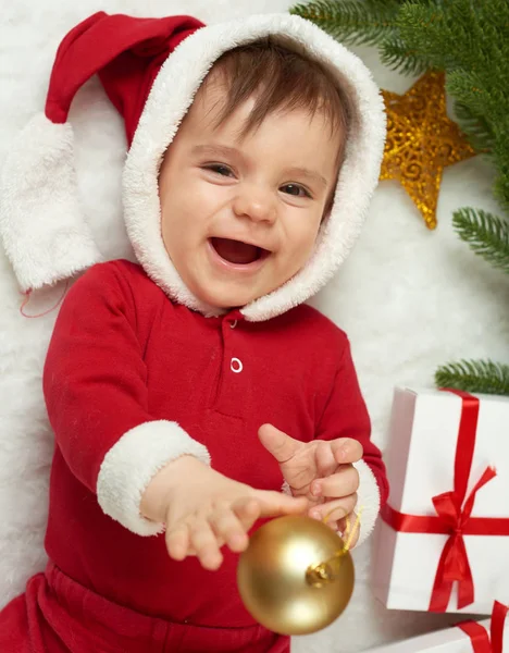 Детский портрет в рождественском украшении, одетый как Санта, лежат на мех возле елки и играть с подарками, зимний праздник концепции — стоковое фото