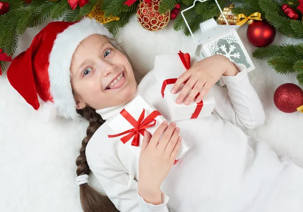 クリスマスの飾り、表情と幸せな感情で楽しんで子供女の子サンタの帽子に身を包んだ、白い毛皮の背景、冬の休日の概念にうそをつく — ストック写真