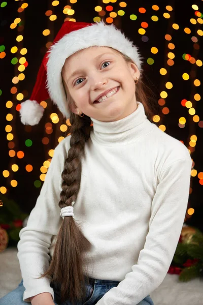 Retrato da menina da criança na decoração de Natal, vestida com chapéu de Santa, luzes boke no fundo escuro, conceito de férias de inverno — Fotografia de Stock