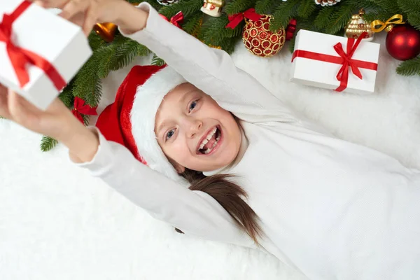 Bambina divertirsi con la decorazione di Natale, espressione del viso e le emozioni felici, vestito con cappello di Babbo Natale, sdraiarsi su sfondo di pelliccia bianca, concetto di vacanza invernale — Foto Stock