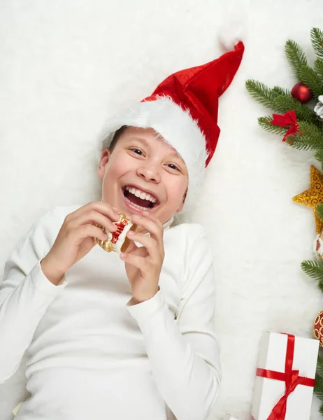 Menino criança se divertindo com decoração de Natal, expressão facial e emoções felizes, vestida com chapéu de Papai Noel, mentira no fundo de pele branca, conceito de férias de inverno — Fotografia de Stock