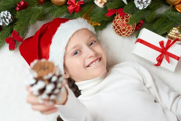 クリスマスの飾り、表情と幸せな感情で楽しんで子供女の子サンタの帽子に身を包んだ、白い毛皮の背景、冬の休日の概念にうそをつく — ストック写真