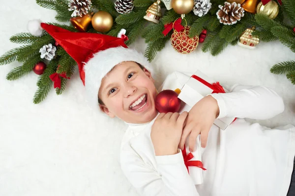 Menino criança se divertindo com decoração de Natal, expressão facial e emoções felizes, vestida com chapéu de Papai Noel, mentira no fundo de pele branca, conceito de férias de inverno — Fotografia de Stock