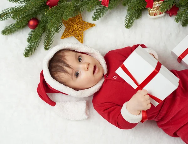 Retrato del bebé en la decoración de Navidad, vestido como Santa, mentira en piel cerca del abeto y jugar con regalos, concepto de vacaciones de invierno — Foto de Stock