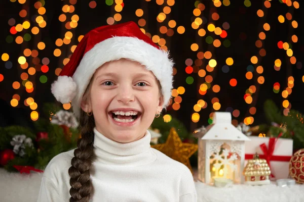 サンタ クロースの帽子とクリスマス デコレーション、照明、表情と幸せな感情、冬の休日の概念で暗い背景に子少女の肖像画 — ストック写真