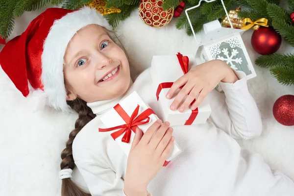 Kind meisje met plezier met Kerstdecoratie, gezicht expressie en gelukkig emoties, gekleed in kerstmuts, liggen op wit bont achtergrond, concept van winter vakantie Rechtenvrije Stockafbeeldingen