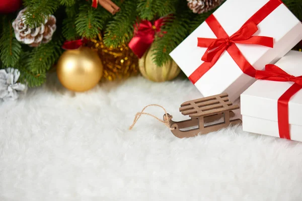 Kerstdecoratie op fir tree branch close-up, houten slee speelgoed, geschenken, xmas bal, kegel en andere objecten op witte lege ruimte bont, concept van de vakantie, plaats voor tekst — Stockfoto