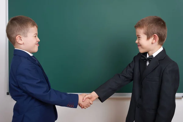 Scuola elementare ragazzo vicino sfondo lavagna vuota, vestito in abito nero classico, allievo di gruppo, concetto di istruzione — Foto Stock