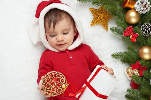 Ritratto del bambino nella decorazione di Natale, vestito da Babbo Natale, sdraiati su pelliccia vicino all'abete e gioca con i regali, concetto di vacanza invernale — Foto Stock
