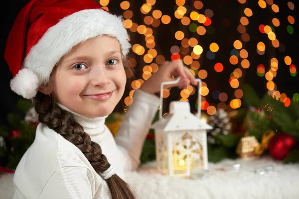 クリスマスの装飾、照明、表情と幸せな感情で暗い背景を持つ子少女の肖像画を着たサンタ帽子、冬の休日の概念 — ストック写真