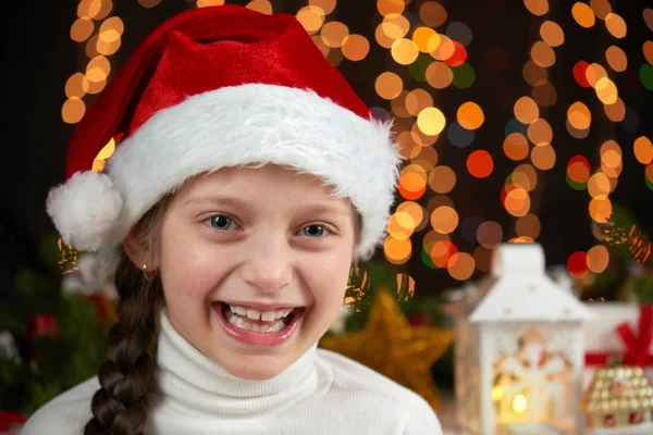 Retrato da menina criança em santa hat com decoração de natal, fundo escuro com luzes, expressão facial e emoções felizes, conceito de férias de inverno — Fotografia de Stock