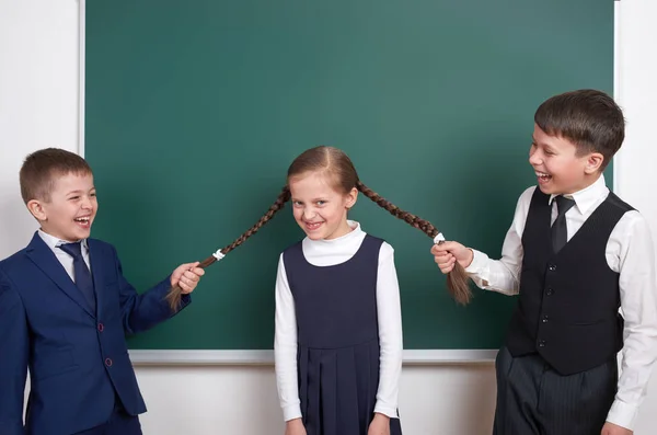 Bambino giocare e divertirsi, ragazzi tirare le trecce ragazza, vicino sfondo lavagna scuola vuota, vestito in abito nero classico, allievo di gruppo, concetto di istruzione — Foto Stock