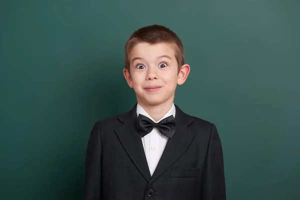 Surpised school boy portrait near green blank chalkboard background, dressed in classic black suit, one pupil, education concept — Stock Photo, Image