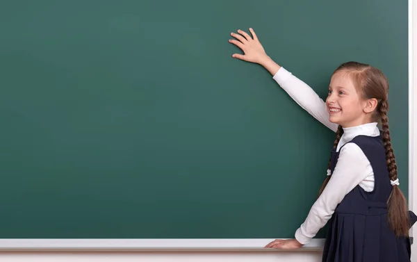 Grundschülerin legt Hände auf Kreidetafel-Hintergrund und zeigt Leerstelle, gekleidet in klassisch schwarzen Anzug, Gruppenschülerin, Bildungskonzept — Stockfoto