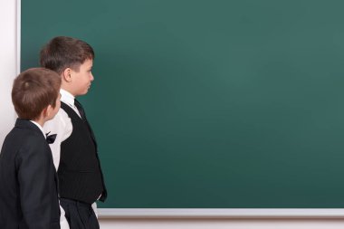 İlköğretim okul çocuk bakmak giyinmiş klasik siyah takım elbise, grup öğrenci, eğitim kavramı boş kara tahta arka plan üzerinde