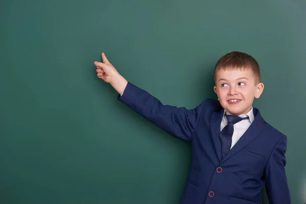Školáka ukázat prstem poblíž prázdnou tabuli pozadí, oblečený v klasickém černém obleku, skupiny žáků, koncepce vzdělávání — Stock fotografie