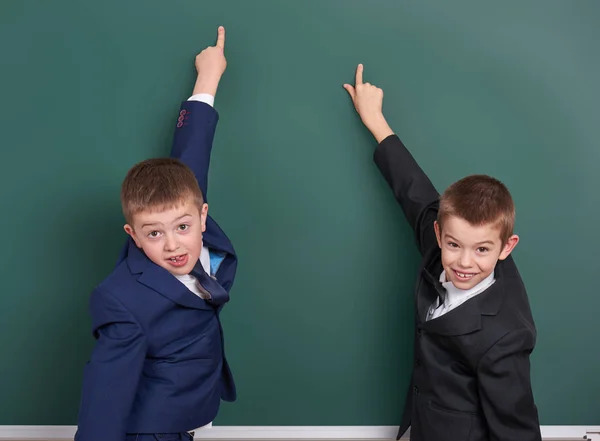 School jongen punt vinger bij leeg schoolbord achtergrond, gekleed in een klassieke zwarte pak, leerling van de groep, onderwijs concept — Stockfoto
