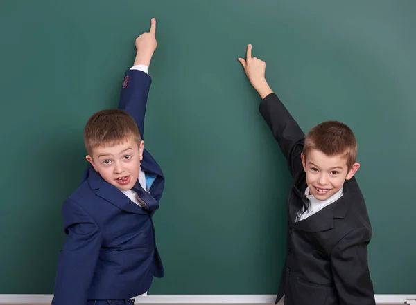 Schuljunge zeigt mit dem Finger auf leeren Tafelhintergrund, im klassischen schwarzen Anzug gekleidet, Gruppenschüler, pädagogisches Konzept Stockbild