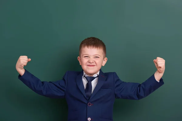 School jongen Toon biceps spieren, portret in de buurt van groene leeg schoolbord achtergrond, gekleed in een klassieke zwarte pak, één leerling, onderwijs concept — Stockfoto