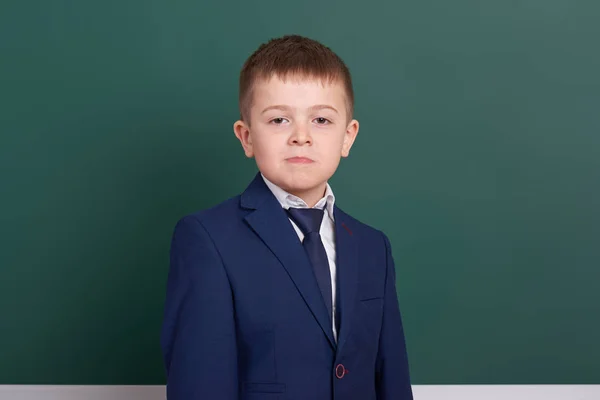 School boy portrait near green blank chalkboard background, dressed in classic black suit, one pupil, education concept — Stock Photo, Image