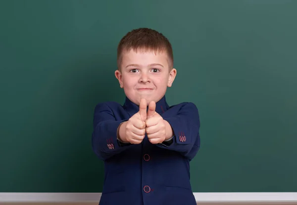School boy show best gesture, portrait near green blank chalkboard background, dressed in classic black suit, one pupil, education concept — Stock Photo, Image