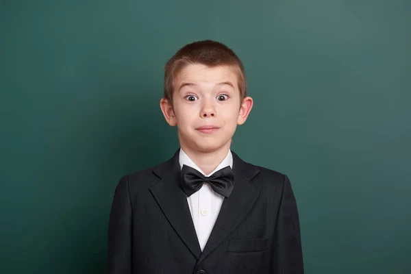 Surpised school boy portrait near green blank chalkboard background, dressed in classic black suit, one pupil, education concept — Stock Photo, Image