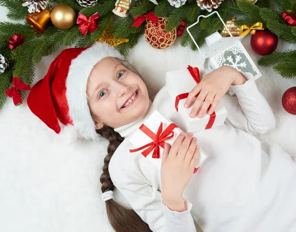 Bambina divertirsi con la decorazione di Natale, espressione del viso e le emozioni felici, vestito con cappello di Babbo Natale, sdraiarsi su sfondo di pelliccia bianca, concetto di vacanza invernale — Foto Stock
