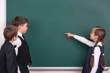 İlköğretim okul erkek ve kız kara tahta arka plan üzerinde el koymak ve boşluk giyinmiş klasik siyah takım elbise, grup öğrenci, eğitim kavramı göstermek