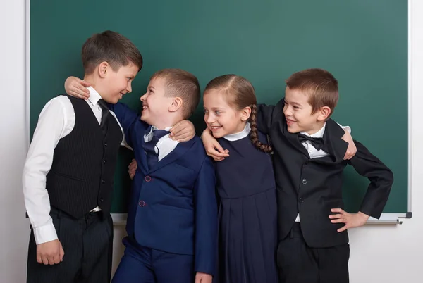 Scuola elementare ragazzo scherzare intorno sfondo lavagna quasi vuota, vestito in abito nero classico, allievo di gruppo, concetto di istruzione — Foto Stock