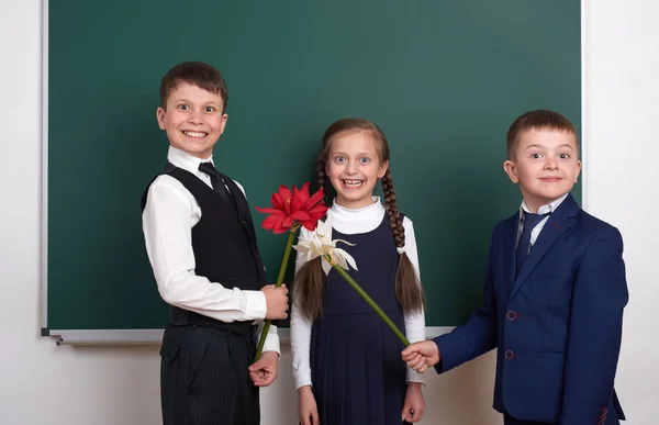 Garçons donnant des fleurs fille, enfant de l'école primaire près de fond de tableau blanc, habillé en costume noir classique, élève de groupe, concept d'éducation — Photo