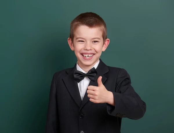 Okul çocuk göstermek en iyi jest, portre yeşil boş kara tahta arka plan, yakınındaki giyinmiş klasik siyah takım elbise, bir öğrenci, eğitim kavramı — Stok fotoğraf