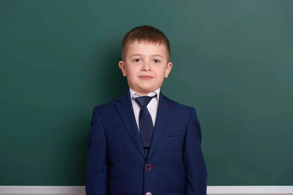 Retrato de niño de escuela cerca de fondo de pizarra verde en blanco, vestido con traje negro clásico, un alumno, concepto de educación — Foto de Stock