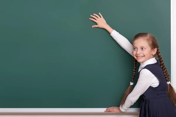 Elementary school girl put hands on chalkboard background and show blank space, dressed in classic black suit, group pupil, education concept — Stock Photo, Image