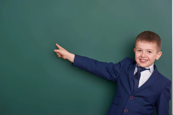 Chico de la escuela señalar el dedo cerca de fondo pizarra en blanco, vestido con traje negro clásico, alumno de grupo, concepto de educación — Foto de Stock