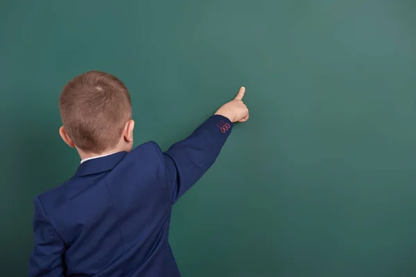 Chłopiec szkoły punkt palcem w pobliżu pusta tablica tło, ubrany w klasyczny czarny garnitur, grupa uczniów, koncepcja edukacji — Zdjęcie stockowe