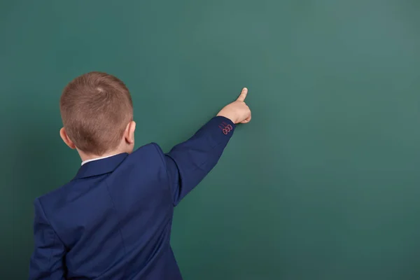 Ragazzo della scuola puntare il dito vicino sfondo lavagna vuota, vestito in abito nero classico, allievo di gruppo, concetto di istruzione — Foto Stock