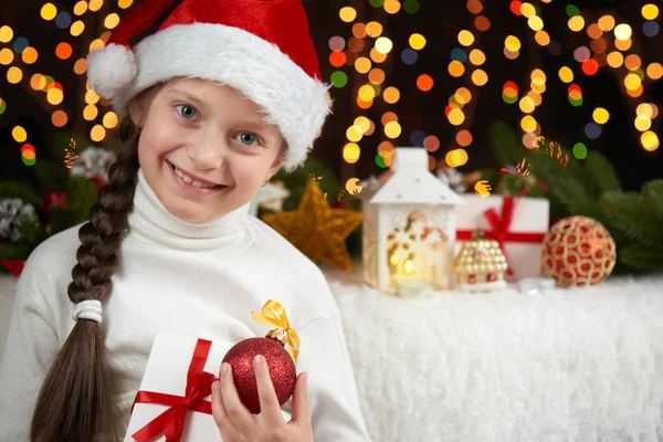 Retrato de niña sobre fondo oscuro con decoración navideña, expresión facial y emociones felices, vestido con sombrero de santa, concepto de vacaciones de invierno — Foto de Stock
